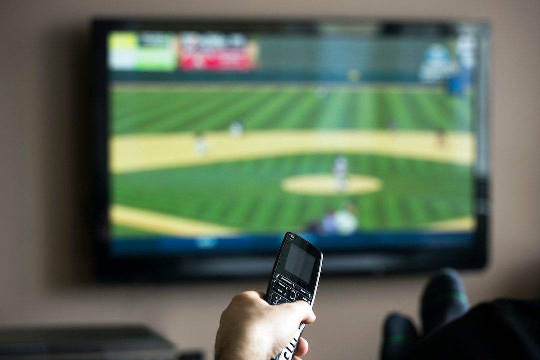 Person watching sports on TV with a universal remote.